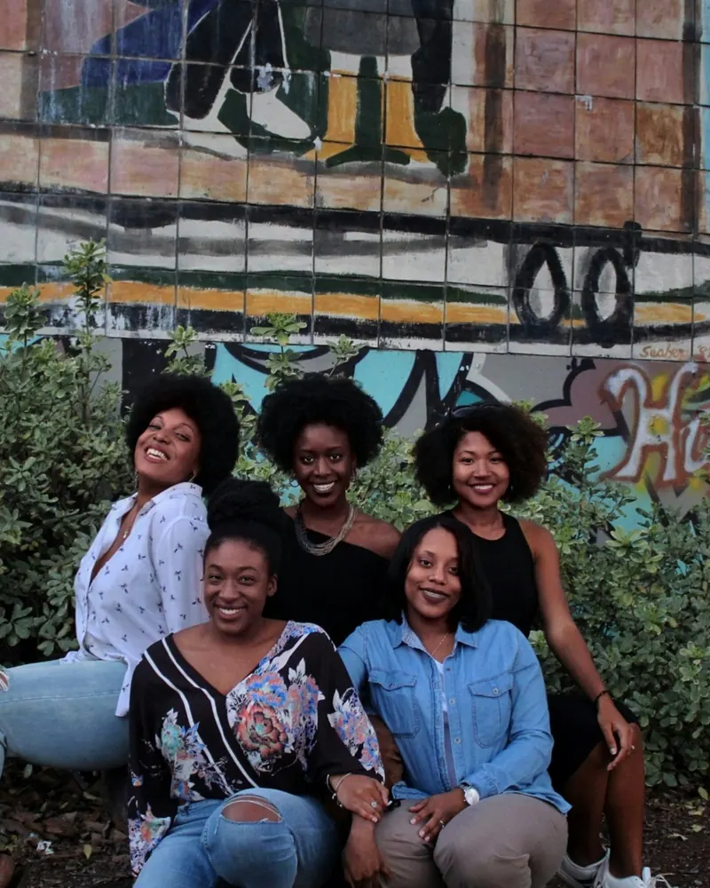 Five friends smiling together in front of a colorful mural