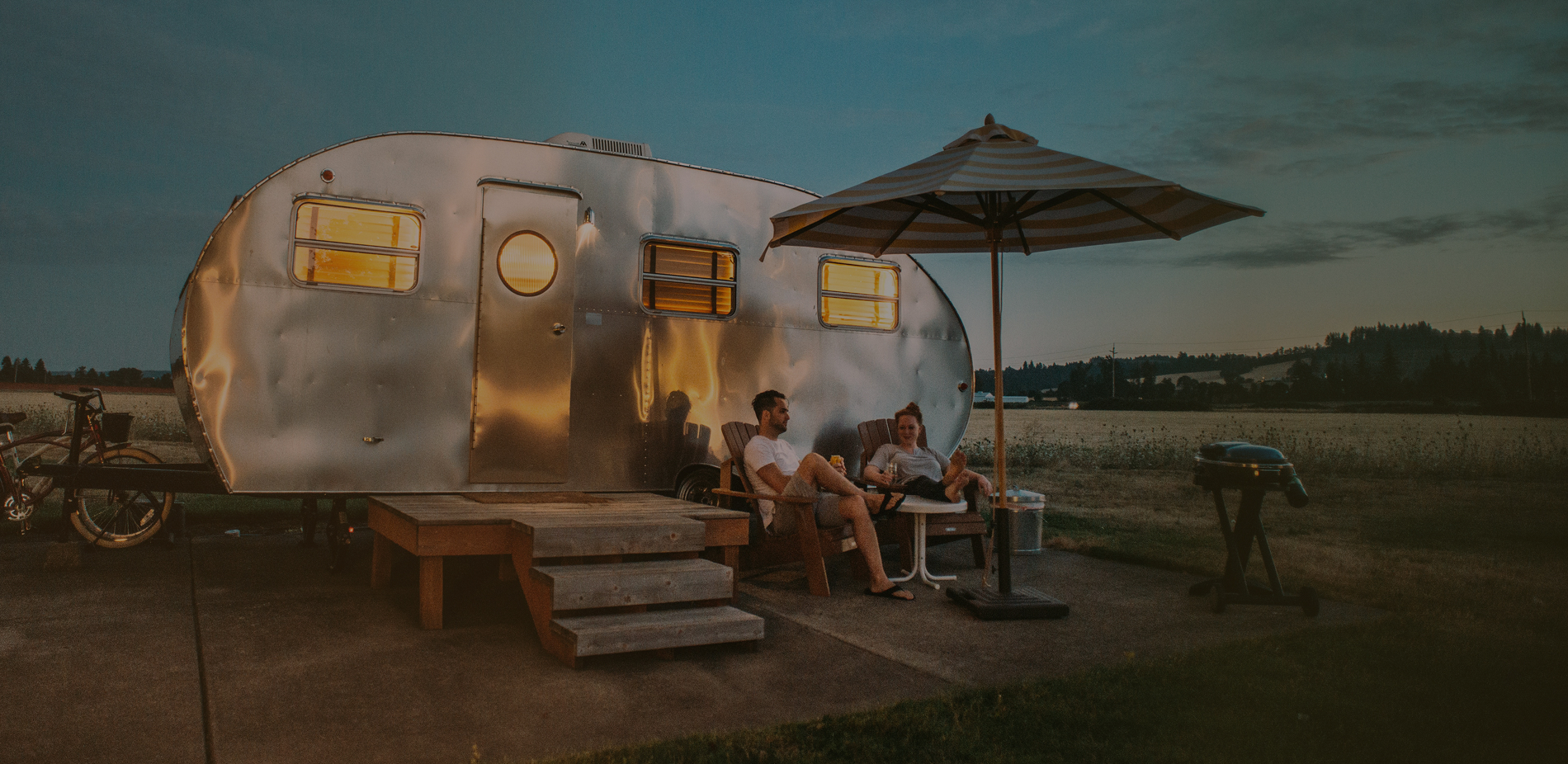 A parked airstream trailer on a campground with a couple enjoying the view.
