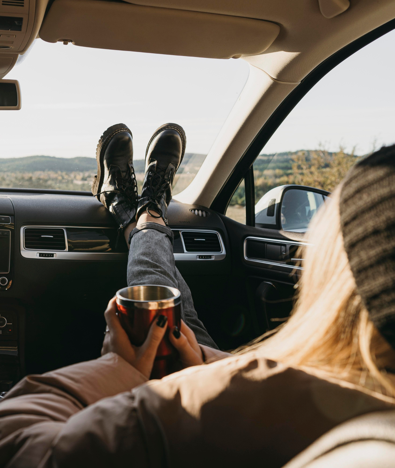 Person relaxing in a car with feet on the dashboard, holding a travel mug, symbolising peace of mind and freedom with a vehicle warranty subscription.