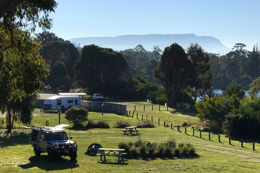Grassy camp sites at Snug Beach Cabin and Caravan Park with kunanyi / Mount Wellington behind