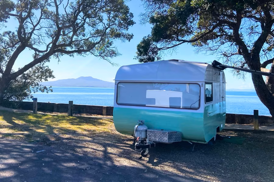 Vintage caravan on a beachfront site at Takapuna Beach Holiday Park with Rangitoto Island across the water