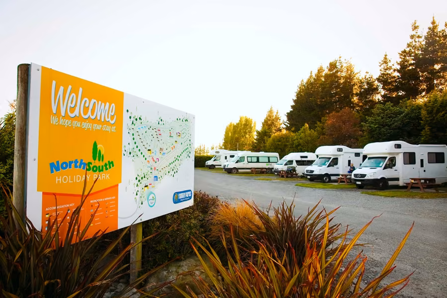 Welcome sign and rental campervans on sites at North South Holiday Park near Christchurch Airport