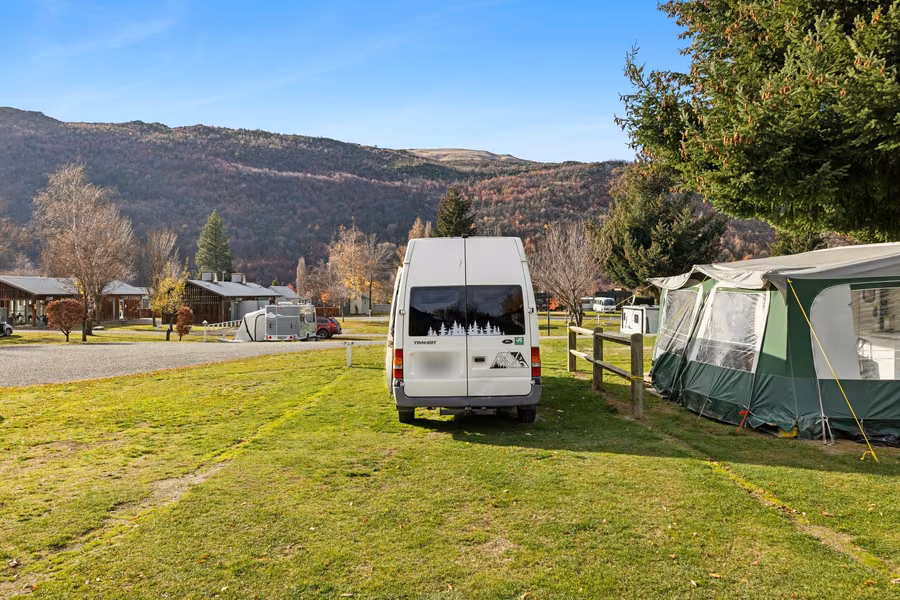 Campervan on a grassy site with autumn hills behind at Arrowtown Holiday Park