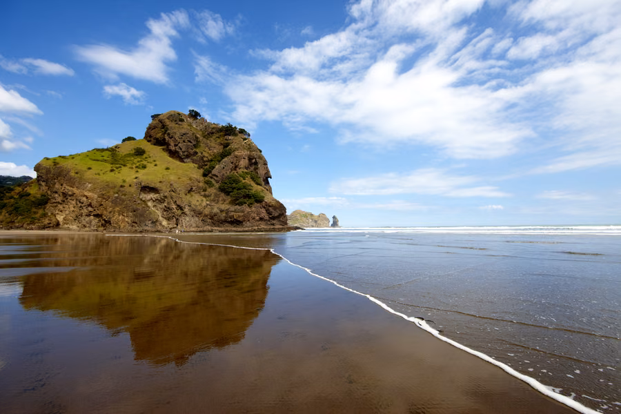 Lion Rock reflected in the wet black sand at Piha on Auckland's west coast