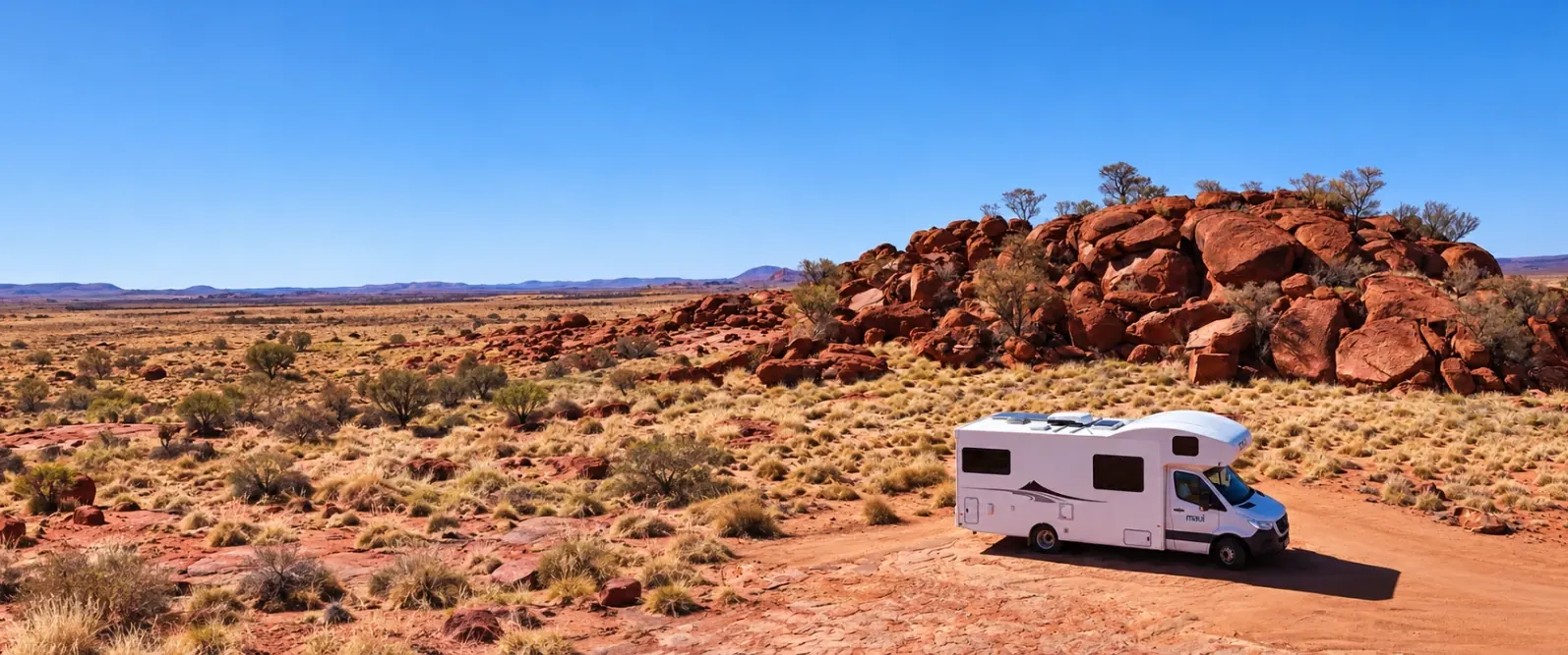 maui motorhome parked on a red dirt track beside a rocky outcrop and spinifex in the Red Centre outback