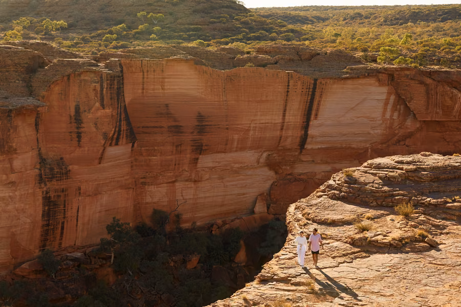 Sheer sandstone wall of Kings Canyon in Watarrka National Park, with two walkers on the rim