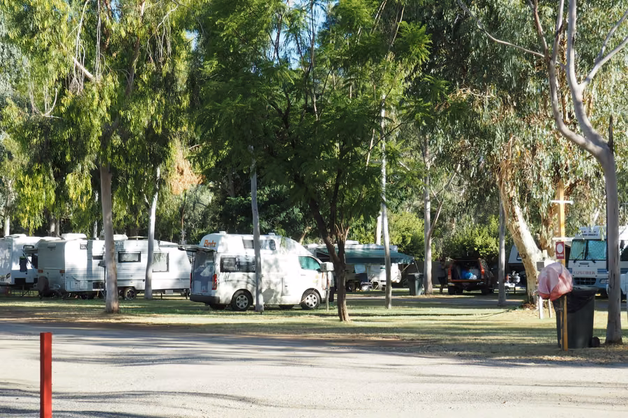 Campervans and caravans on shady, grassed sites under gum trees at Heritage Caravan Park, Alice Springs