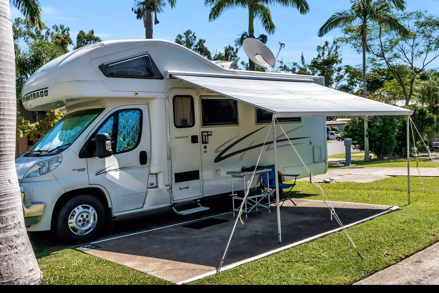 Motorhome with its awning out on a powered site under palm trees at Discovery Parks - Airlie Beach