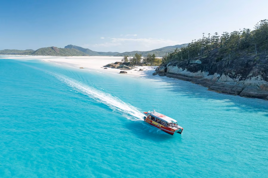 Tour boat speeding across turquoise water at Hill Inlet with the white sands of Whitehaven Beach behind