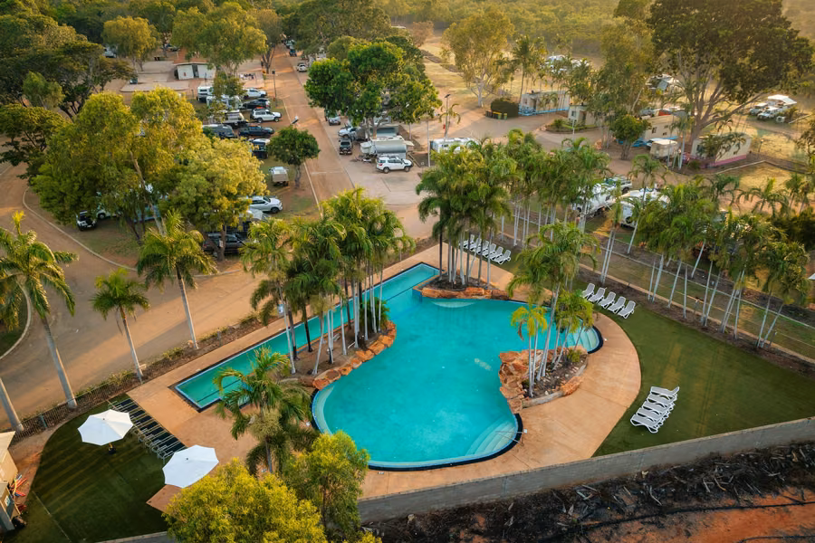 Aerial view of the palm-fringed lagoon pool and lap pool beside shaded caravan sites at Broome Caravan Park