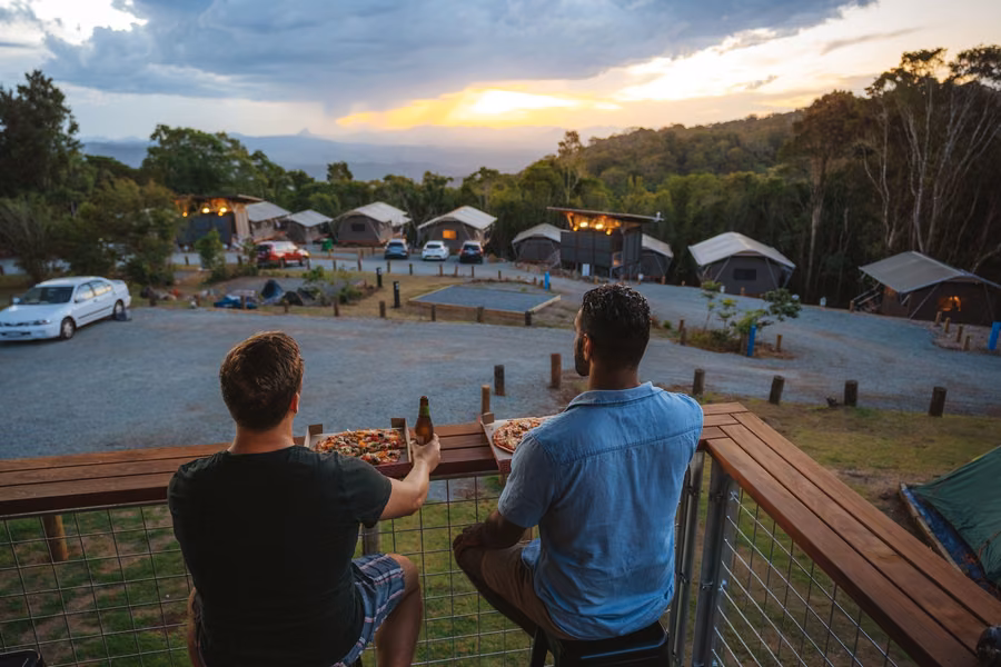 Two campers on a deck looking over the safari tents at O'Reilly's Campground in Lamington National Park at sunset