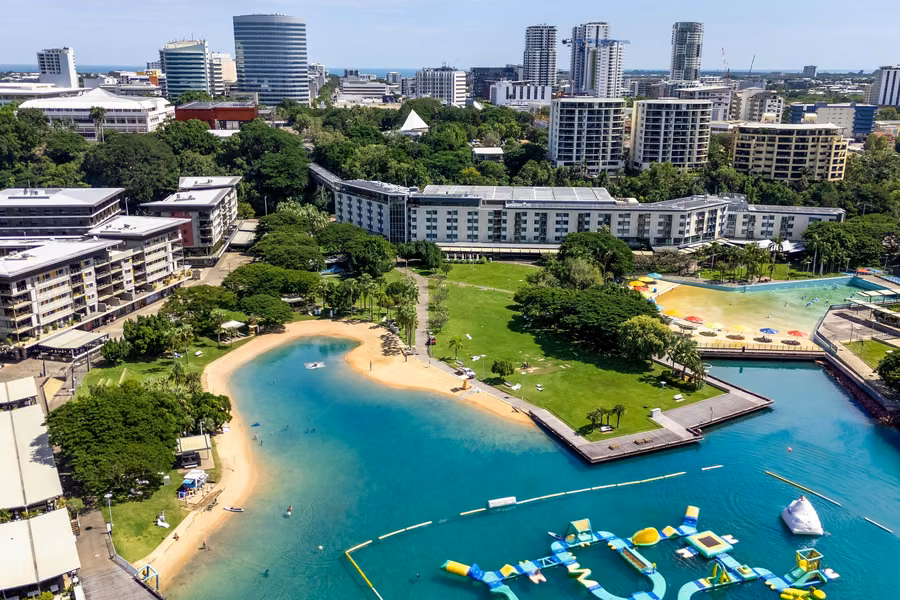 Aerial view of the Darwin Waterfront's lagoon beach, lawns and aqua park, with city buildings behind