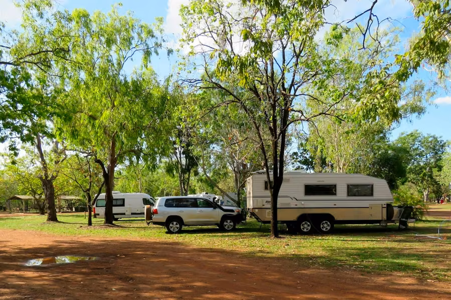 Campervan, 4WD and caravan parked on grassy sites under shady trees at the Cooinda campground in Kakadu