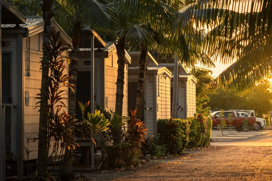Row of cabins under palm trees in golden evening light at Discovery Parks Darwin, with tropical plants along a gravel road
