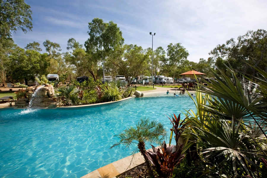 Landscaped pool with a rock waterfall at Nitmiluk campground, with motorhomes parked on sites among the trees behind