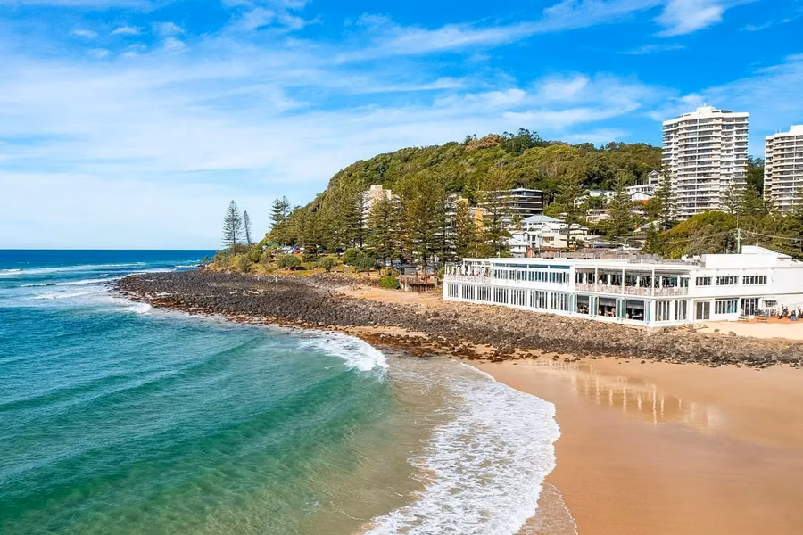 Aerial view of Burleigh Beach curving to the forested headland of Burleigh Head National Park, with the pavilion on the foreshore