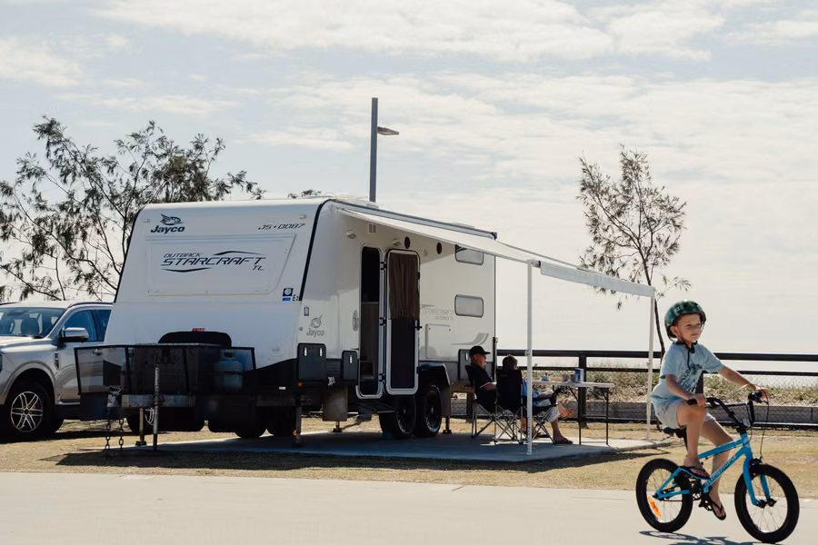 Child riding a bike past a caravan with its awning out on a beachfront site at Tweed Holiday Parks Kingscliff Beach