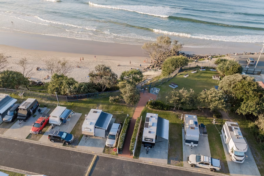 Aerial view of caravans and campers on powered slab sites behind the beach at First Sun Holiday Park in Byron Bay