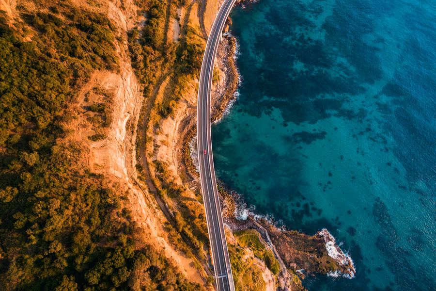 Aerial view of Sea Cliff Bridge curving around the sandstone cliffs above turquoise water on the Grand Pacific Drive