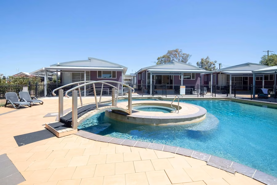 Resort-style pool with an arched footbridge to a round spa, sun loungers and cabins behind at Ingenia Holidays Hunter Valley