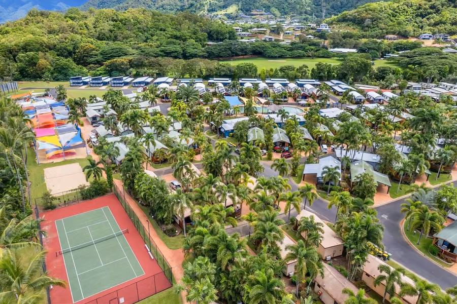 Aerial view of BIG4 Ingenia Holidays Cairns Coconut, with caravan sites, cabins, palm trees and a tennis court below green hills