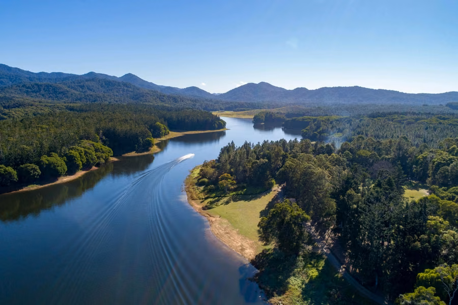 Aerial view of a boat leaving a wake across Lake Tinaroo between forested shores, with Atherton Tablelands ranges beyond