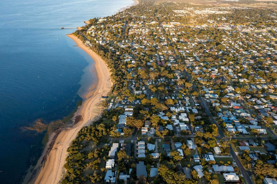 Aerial view of the Cowes foreshore on Phillip Island, with holiday park sites among trees behind a long sandy beach