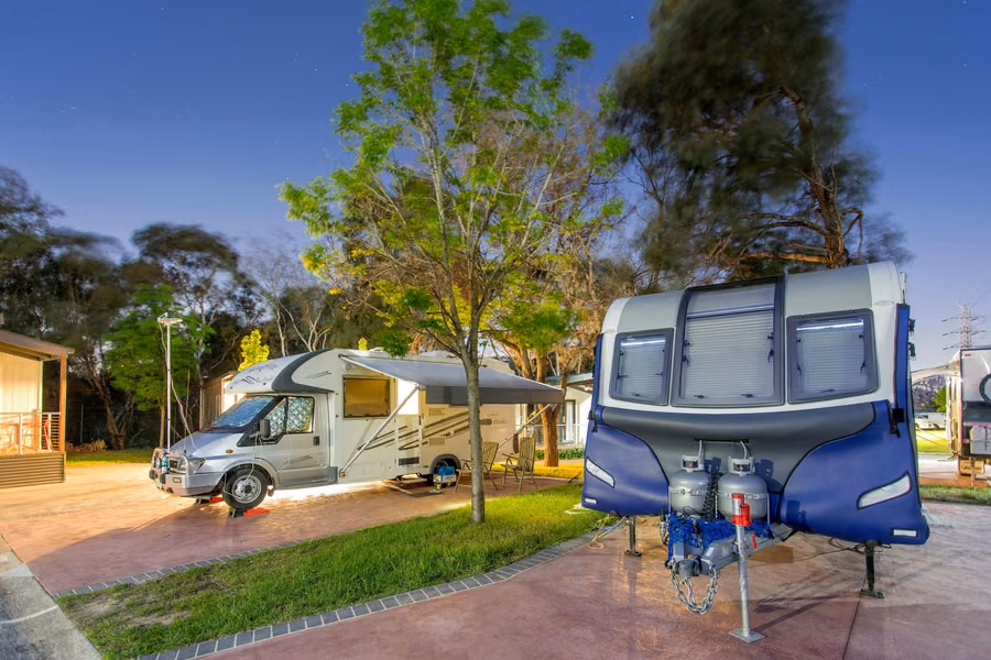 Motorhome with its awning out on a paved powered site at dusk, beside a caravan, at BIG4 Melbourne Holiday Park
