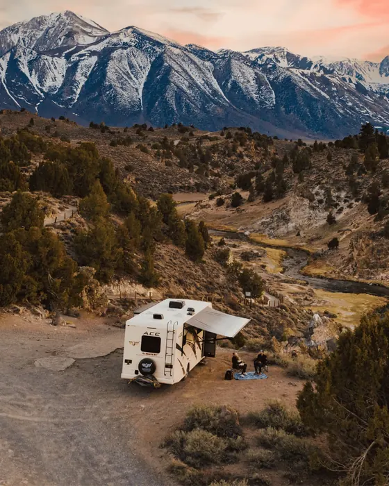 Truck camper with its awning out in a desert valley below snow-capped mountains in the USA