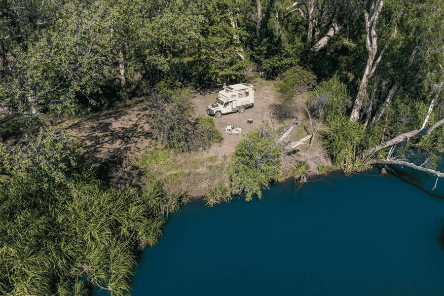 Aerial view of a 4WD truck camper parked at a private bush campsite above a deep green river at El Questro