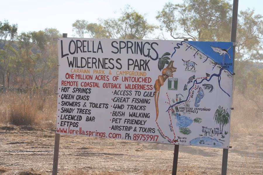 Hand-painted Lorella Springs Wilderness Park sign with a map, listing hot springs, 4WD tracks and Gulf access, beside a dusty outback track