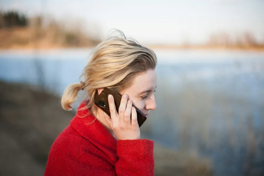 Traveller in a red coat talking on her phone beside a lake