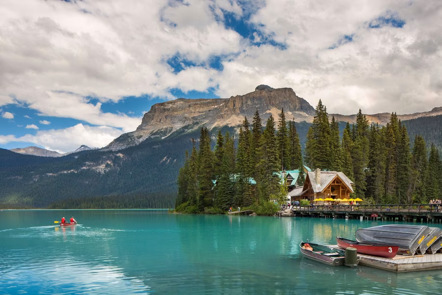 Red canoe on the green water of Emerald Lake near Emerald Lake Lodge and its canoe dock, with forest and a rocky peak behind