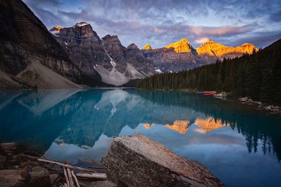 Moraine Lake reflecting the Valley of the Ten Peaks, with the summits glowing orange and a boulder in the foreground