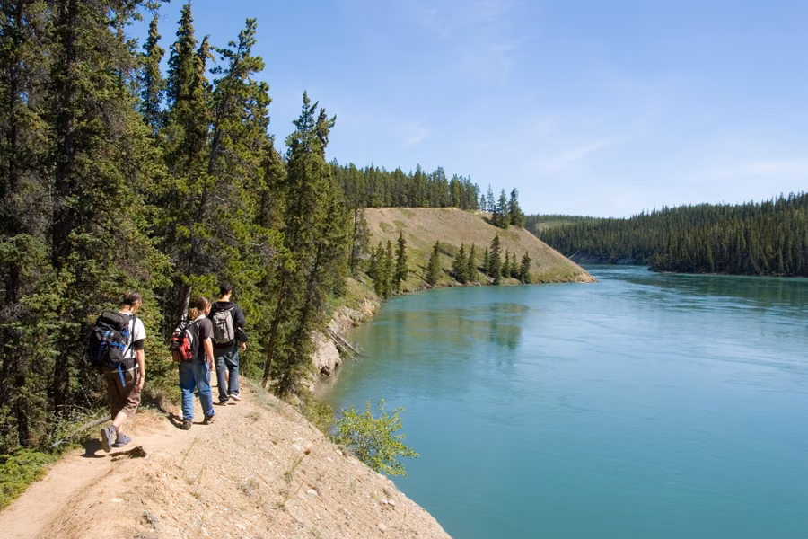 Hikers on the trail along the rim of Miles Canyon above the turquoise Yukon River near Whitehorse