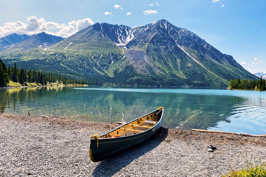 Canoe on the gravel shore of Kathleen Lake, with forested mountains rising beyond the turquoise water