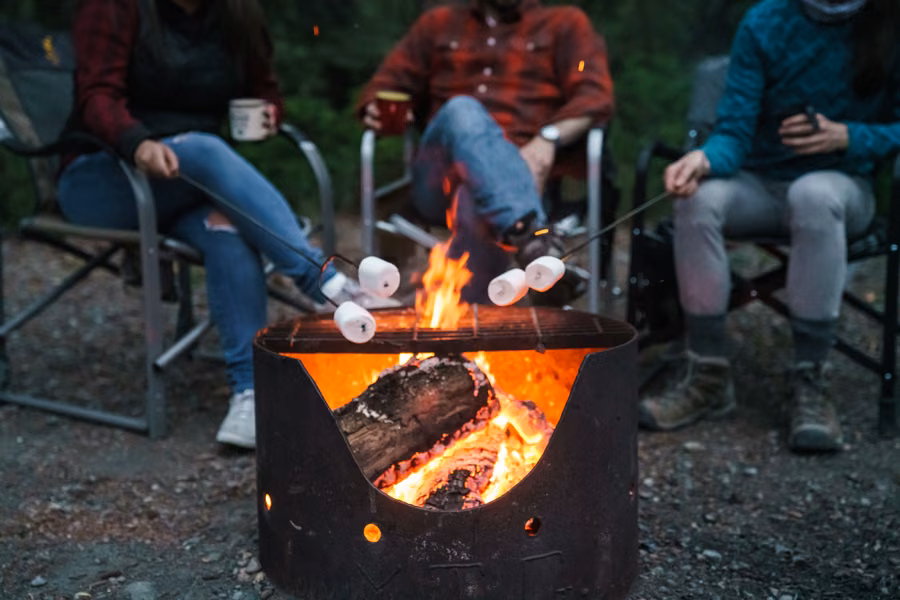Campers toasting marshmallows over a steel fire ring at a Yukon government campground