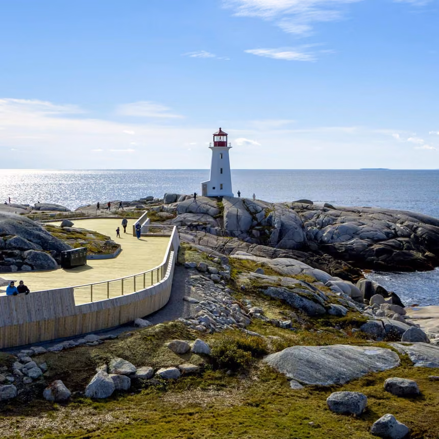 Peggy's Point Lighthouse on granite rocks above the Atlantic, with visitors on the curved viewing deck at Peggy's Cove