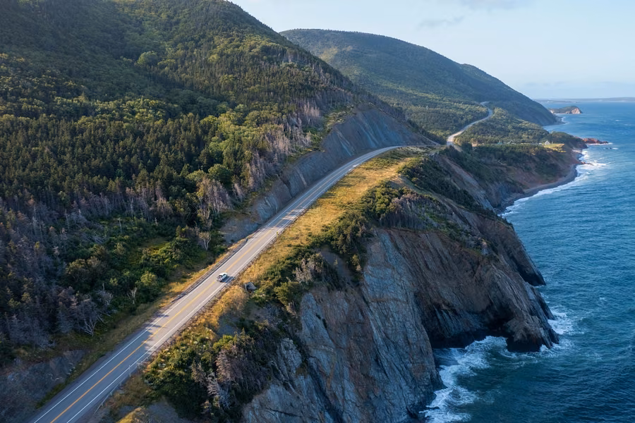 Aerial view of the Cabot Trail running along a clifftop above the ocean, with green highlands behind
