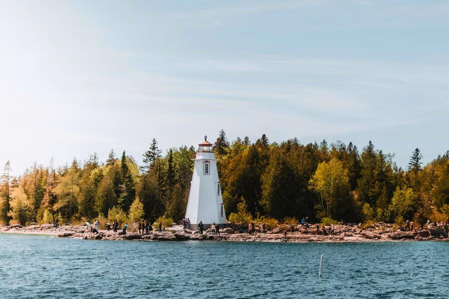White Big Tub Lighthouse on the rocky shore at Tobermory, backed by autumn trees