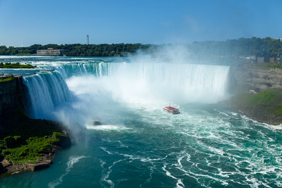 Red tour boat heading into the mist at the foot of the curving Horseshoe Falls, seen from above the Niagara River gorge