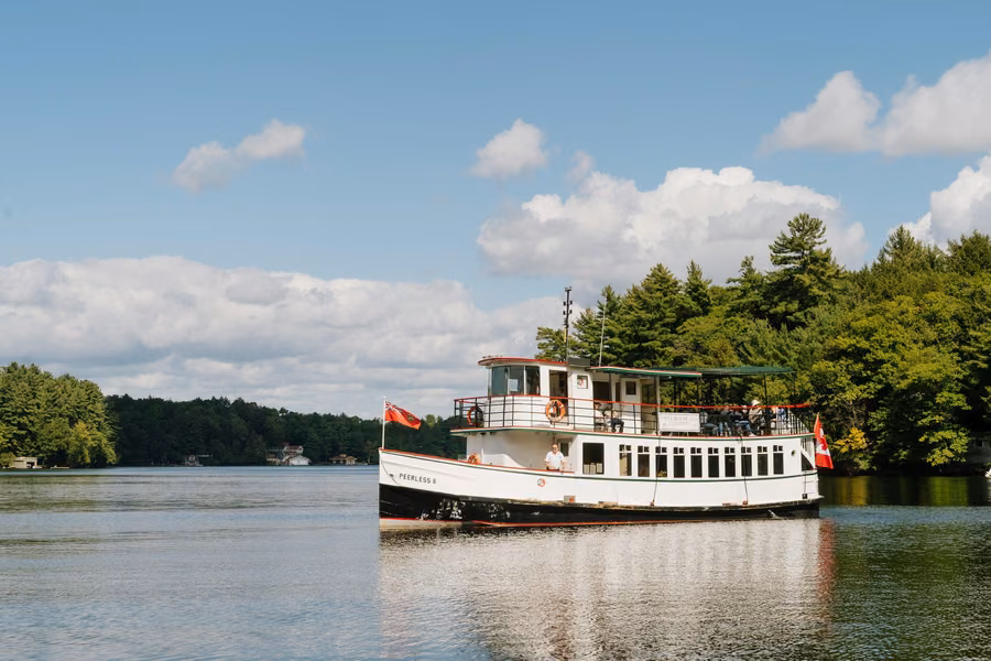 The Peerless II cruise boat flying Ontario and Canadian flags on a tree-lined Muskoka lake