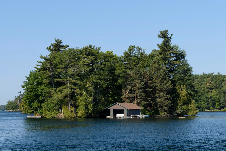 Pine-covered island with a boathouse on the St. Lawrence River, seen from Ivy Lea in the Thousand Islands