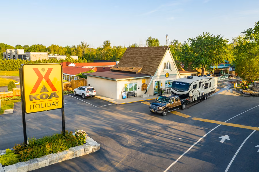 Fifth-wheel caravan and pickup truck pulling up beside the office and KOA Holiday sign at Niagara Falls KOA Holiday