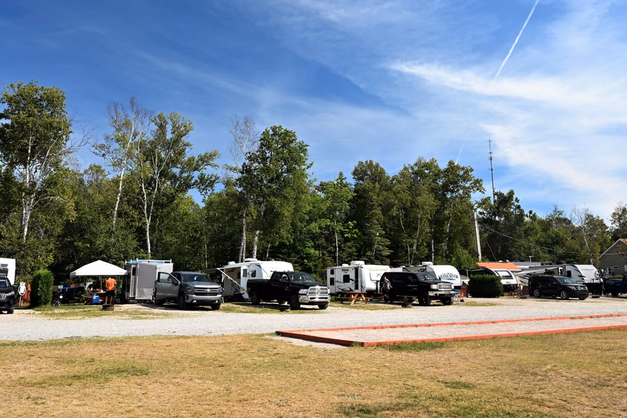 Row of RVs, trailers and pickups on gravel sites under birch trees at Camping Tadoussac on a sunny day