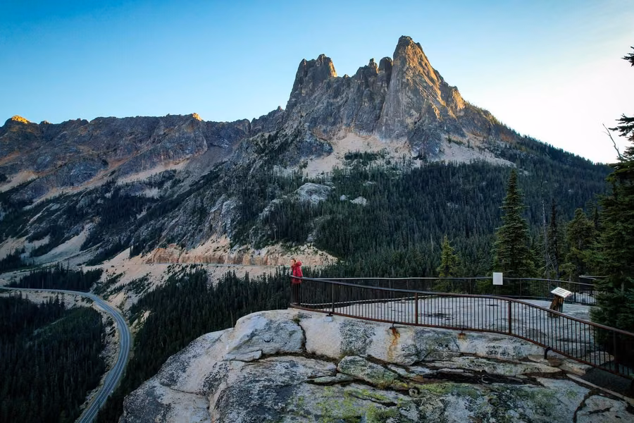Washington Pass Overlook on a granite outcrop below jagged peaks, with the North Cascades Highway curving through the forest