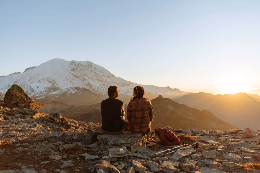 Couple sitting on a rocky ridge watching the sunset light on snow-covered Mount Rainier