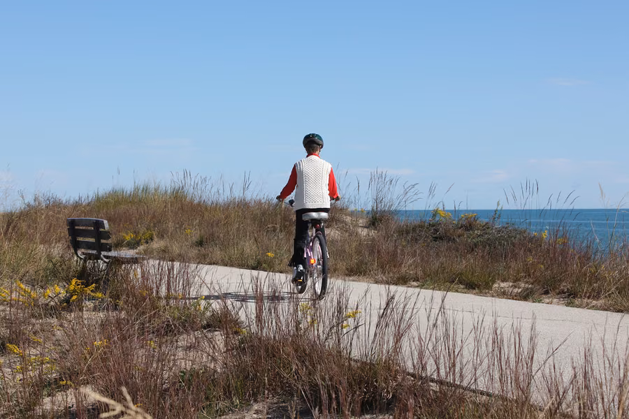 Cyclist riding a paved trail through dune grasses beside Lake Michigan at Illinois Beach State Park