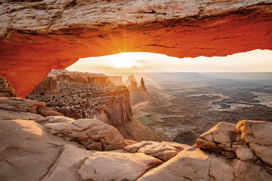 Sunrise glowing beneath Mesa Arch above a deep canyon in Canyonlands National Park