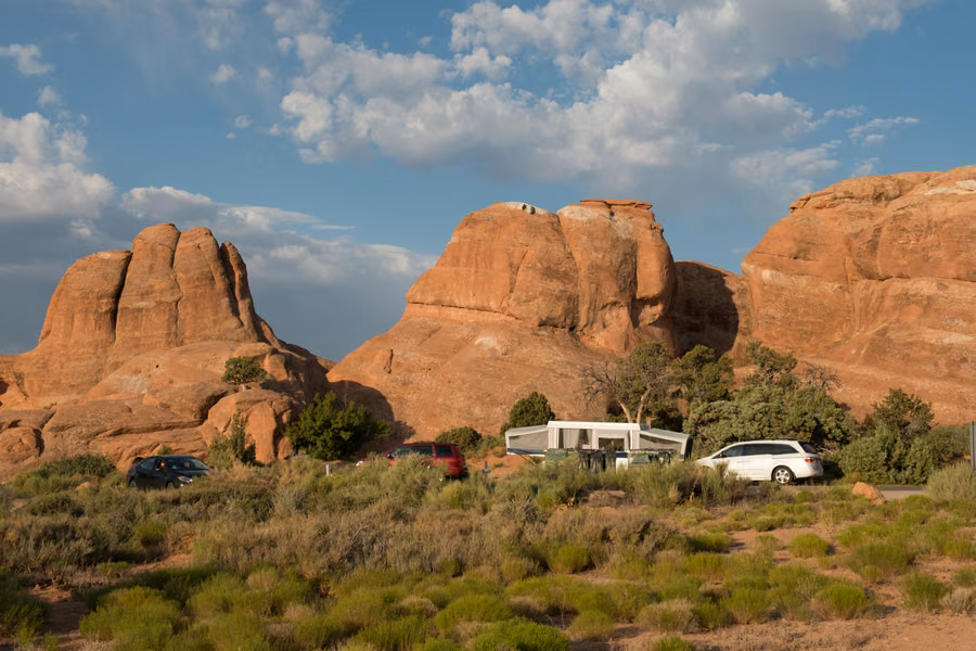 Pop-up camper and cars parked at Devils Garden Campground below red sandstone domes in Arches National Park